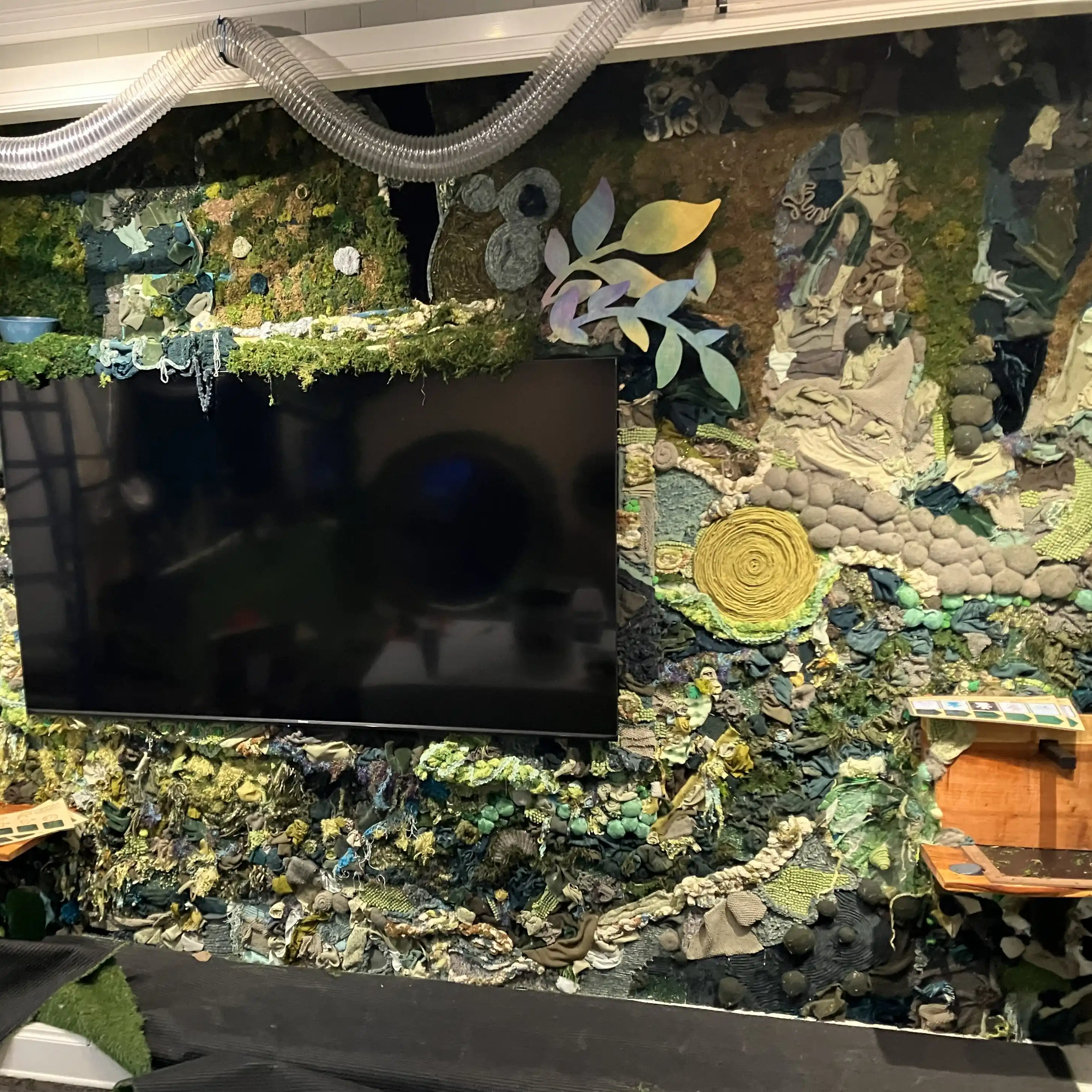 Large wall decorated with green fabrics, with a TV screen in the middle